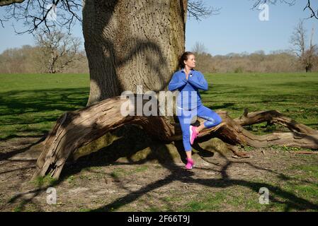 Eine Frau mittleren Alters, die Übung nimmt. Baum Pose in Yoga unter und Eiche. Stockfoto