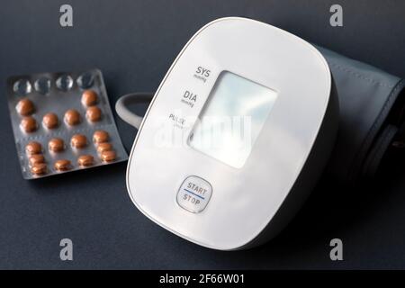 Automatischer Blutdruck-Monitor und Blister mit Pillen auf dunkelgrauem Hintergrund. Medizinischer elektronischer Tonometer Stockfoto