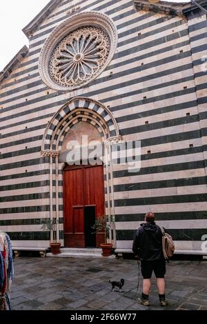 Junger Erwachsener Mann mit einem kleinen Hund vor der Kirche von San Giovanni Battista - Schwarz-Weiß-Fassade in Monterosso al Mare, Cinque Terre, I Stockfoto