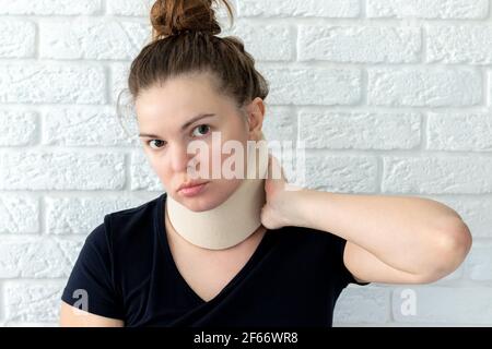 Frau mit zervikalen chirurgischen Kragen vor einem verschwommenen weißen Backstein Wand Hintergrund. Stockfoto