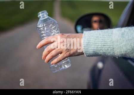 Umwelt nicht mit Plastik verschmutzen! Die Hand des Fahrers hält die Plastikflasche vom Autofenster. Umweltschutz Stockfoto