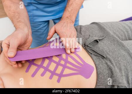 Teilansicht des Physiotherapeuten, der Kinesioband auf der Rückseite des aufführt Frau Stockfoto