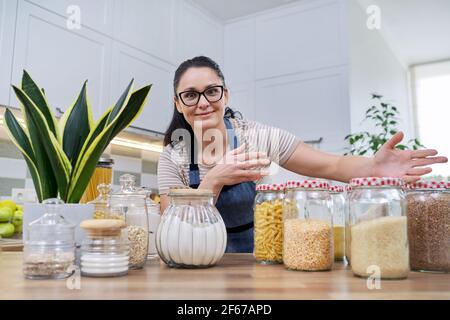 Lagern von Lebensmitteln in der Küche, Frau mit Gläsern und Behältern reden und Blick auf die Kamera Stockfoto