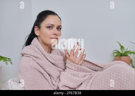 Schöne Frau sitzt zu Hause unter gestrickten warmen Decke mit tasse Tee Stockfoto