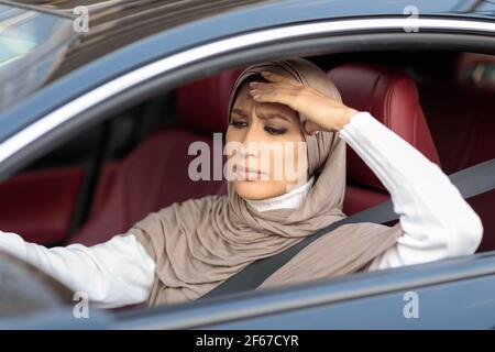 Verärgerte muslimische Frau, die allein in ihrem neuen Auto fährt Stockfoto