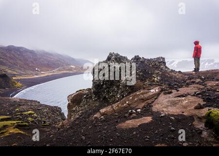 Tourist steht auf einem Felsen und blickt auf den schwarzen Strand Des Kleifarvatn-Sees bei Krysuvik in Island Stockfoto