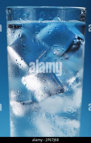 Eiswürfel in einem vernebelten Glas mit Tropfen Eiswasser Nahaufnahme Makro. Erfrischendes und kühlendes Getränk bei heißem Wetter. Blauer Hintergrund. Vollbild Stockfoto