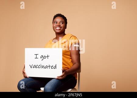 Happy Black Woman zeigt Poster Ich wurde geimpft, Beige Hintergrund Stockfoto