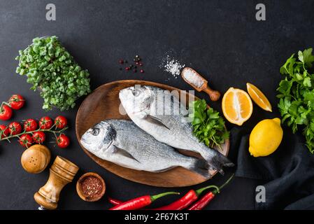 Zwei frische dorado-Fische und Zutaten zum Kochen auf schwarzem Schieferhintergrund, Draufsicht mit Kopierraum für Text- oder Designelemente. Roher Fisch, ungekocht Stockfoto