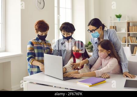 Schüler und Lehrer in medizinischen Gesichtsmasken coding Spiel Auf einem Laptop-Computer Stockfoto