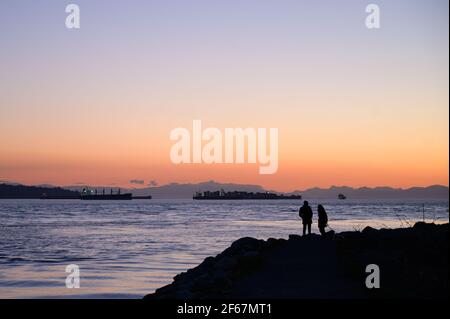 Ein Paar beobachtet den Sonnenuntergang vom Ambleside Park in West Vancouver. West Vancouver, British Columbia, Kanada. Stockfoto