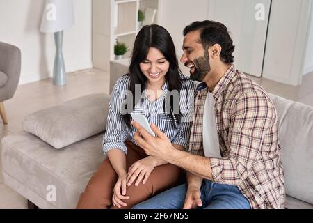 Glückliches junges indisches Paar lachend Blick auf Smartphone zusammen zu Hause. Stockfoto