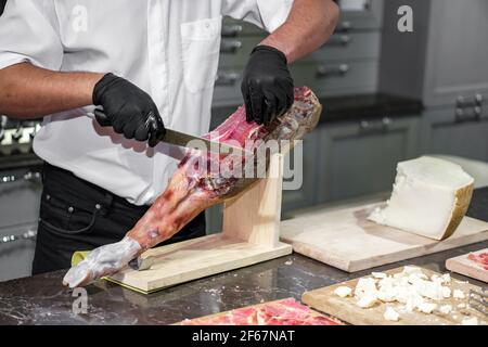 Ein Mann schneidet ruckartig mit einem Messer. Jamon- oder parmaschinken auf Holzständer Stockfoto