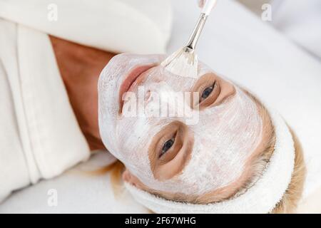 Nahaufnahme Foto der Kosmetikerin Anwendung Ton Gesichtsmaske auf Gesicht einer älteren Frau Stockfoto