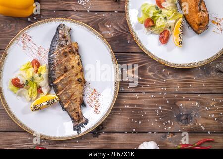 Gegrillter Fisch auf einem Teller mit Gemüse, Paprika, grobes Salz auf braunem Holzgrund. Restaurant-Service. Stockfoto