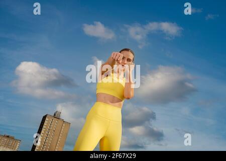 Frau trägt gelbe activewear Ausübung ouside in einer städtischen Umgebung, Fäuste in einem Boxen Pose. Stockfoto