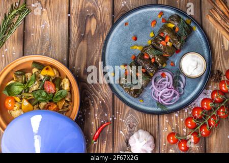 Dolma in Traubenblättern auf einer Platte auf braunem Holzhintergrund, dekoriert mit Gewürzen, Chilischoten, Kirschtomaten. Ein Gericht der Speisekarte des Restaurants. Stockfoto