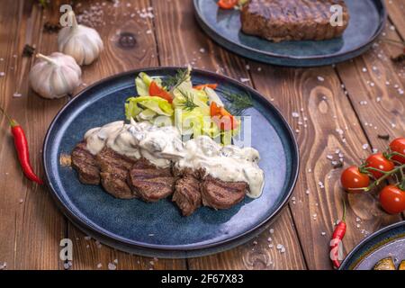 Rinderpastete auf einer Platte mit Gemüse, Salat, Paprika, Rosmarin, Knoblauch und Sesam auf braunem Holzgrund. Restaurant-Service. Stockfoto