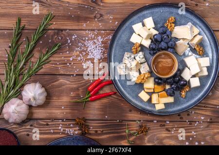 Ein Teller mit Käse, Honig, Trauben auf Holzgrund, mit Gewürzen, Rosmarin, Knoblauch verziert. Restaurant-Service. Stockfoto