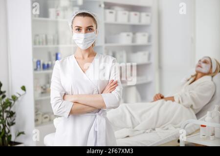 Weibliche Beauty-Arzt steht trägt Gesichtsmaske, während Geduld legen auf den Hintergrund mit Creme oder Maske, in der Kosmetik-Klinik Stockfoto