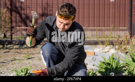 Unschärfe junge Bauarbeiter mit geschwollenen Wangen in gelben Gläsern entfernen Unregelmäßigkeiten auf Boden Estrich mit Hammer und Meißel. Männliche Hände in re Stockfoto