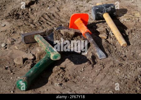 Unschärfe-Hammer, Hammer, Meißel und Bajonett der Schaufel liegen auf dem Boden. Set von Werkzeugen für die Verlegung von Pflastersteinen. Grundlegende Werkzeuge zum Abreißen und Reparieren Stockfoto