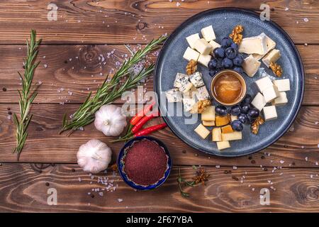 Ein Teller mit Käse, Honig, Trauben auf Holzgrund, mit Gewürzen, Rosmarin, Knoblauch verziert. Restaurant-Service. Stockfoto