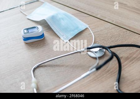 Stethoskop, Fingerspitzenpulsoximeter und medizinische Maske liegen auf einem Holztisch. Draufsicht. Stockfoto