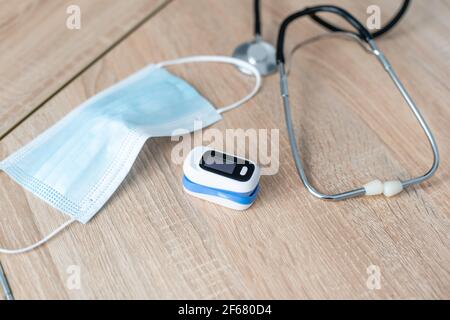 Stethoskop, Fingerspitzenpulsoximeter und medizinische Maske liegen auf einem Holztisch. Draufsicht. Stockfoto