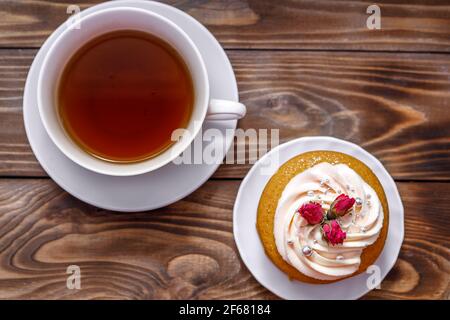 Biskuitkuchen mit Sahne, verziert mit kleinen Blumen und einer Tasse Tee. Das Konzept eines festlichen Leckerbissen. Handarbeit Stockfoto