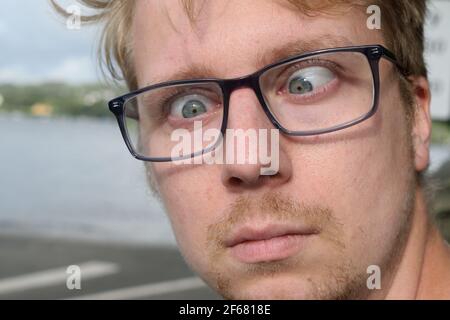 Ein junger Mann in einer Brille, der ein dummes Gesicht mit gekreuzten Augen zieht Stockfoto
