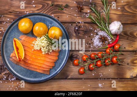 Forellenscheiben auf einem Teller, frische Brötchen, Orange, Chili, Kirschtomaten, Rosmarin auf braunem Holzgrund. Das Konzept des Restaurant-Service. Stockfoto