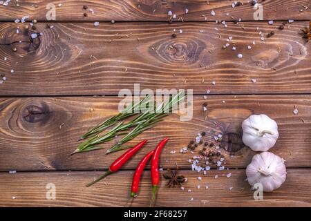 Chilischote, Knoblauchköpfe, grobes Salz und Rosmarin auf braunem Holzgrund. Stockfoto