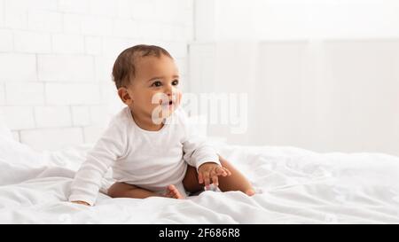 Afrikanisches Baby Kleinkind Sitzt Auf Dem Bett Und Schaut Im Schlafzimmer Zur Seite Stockfoto