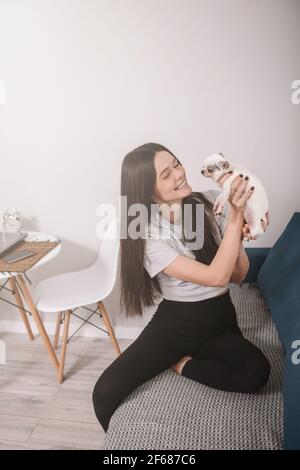 Vertikales Porträt einer glücklichen schönen Frau mit entzückenden kleinen chihuahua Hund, zu Hause auf dem Sofa sitzen Stockfoto