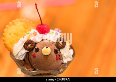 Japanisches Dessert in einem Glas mit Eiscreme in Form eines niedlichen Bären in Schokolade mit süßer Schlagsahne, Keksen und cher gekrönt Stockfoto