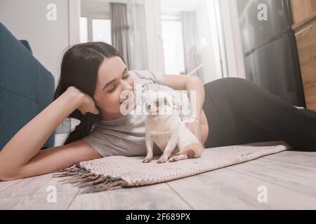 Glückliche gesunde Frau, die mit ihr auf dem Boden liegt Hund zu Hause Stockfoto