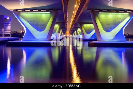 Wunderschöne Aussicht auf die berühmte blau beleuchtete Al Garhoud Brücke in Dubai, Vereinigte Arabische Emirate mit den bunten Spiegelungen auf dem Wasser Stockfoto