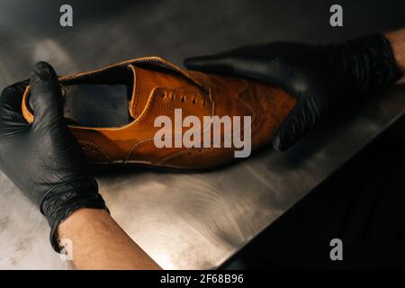 Nahaufnahme der Hände eines schwarz getragenem Schuhmacherschuhrers von oben Handschuhe fügen in abgenutztes hellbraunes Leder eine Schuhunterlage aus Holz ein Schuhe Stockfoto