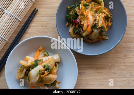 Zwei Schüsseln koreanischer Kimchee neben einer Sushi-Rolle Matte und Essstäbchen Stockfoto