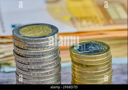 Stapel von ein und zwei Euro-Münzen vor europäischen Banknoten, im Hintergrund verschwommen Stockfoto