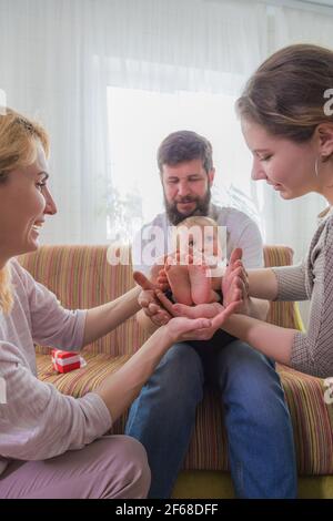 Die ganze Familie, Eltern und Kinder halten die Fersen des Babys in den Handflächen. Stockfoto