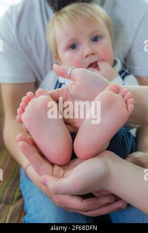 Die ganze Familie, Eltern und Kinder halten die Fersen des Babys in den Handflächen. Stockfoto