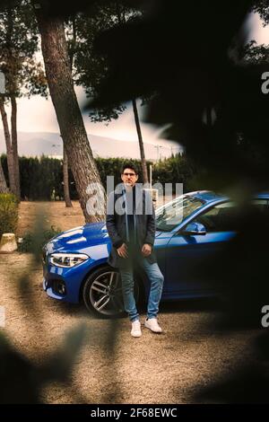 Junger Mann, der vor seinem blauen Auto sitzt Warten Stockfoto