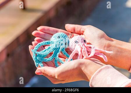 Gestrickte Spielzeugschlüsselanhänger, blau und rosa gestrickte Krake Schlüsselanhänger an einer weiblichen Hand close-up Stockfoto