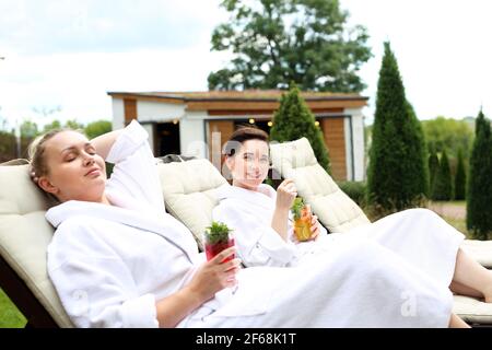 Pärchen sonnen sich auf den Sonnenliegen. Frauen entspannen sich in einem luxuriösen Spa. Zwei Frauen entspannen sich an einem sonnigen Sommertag auf Liegestühlen Stockfoto