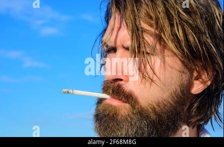 Bärtiger Mann raucht draußen Zigarette. Brutaler Kerl, der Tabak raucht. Medizinisches Cannabis. Stockfoto