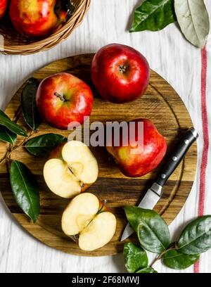 Auf einem Holzchopingbrett auf dem Küchentisch liegend frisch gepflückte, leckere, reife und saftige rote Äpfel, geschnitten, um als gesunder Snack genossen zu werden. Stockfoto