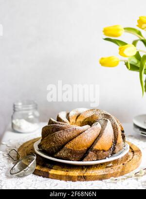 Ostertisch mit frisch gebackenem, veganen, traditionellen polnischen Osterbabka-Kuchen - Schicht aus Zitrus- und Schokoladenschwamm, mit Puderzucker gesprenkelt. Stockfoto