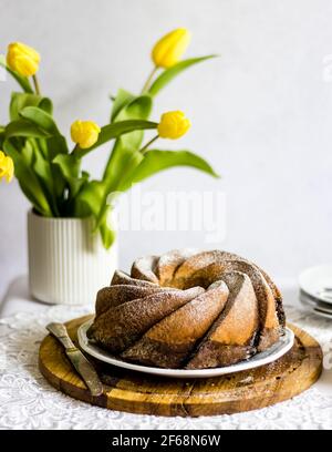 Ostertisch mit frisch gebackenem, veganen, traditionellen polnischen Osterbabka-Kuchen - Schicht aus Zitrus- und Schokoladenschwamm, mit Puderzucker gesprenkelt. Stockfoto